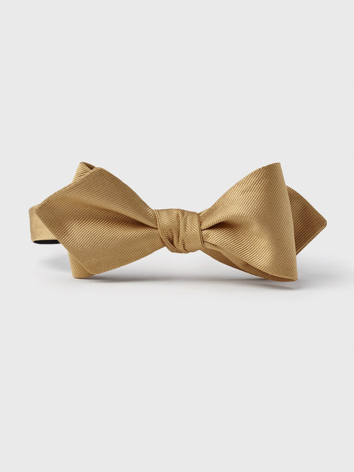 Gold bow tie with a textured fabric on a white background.