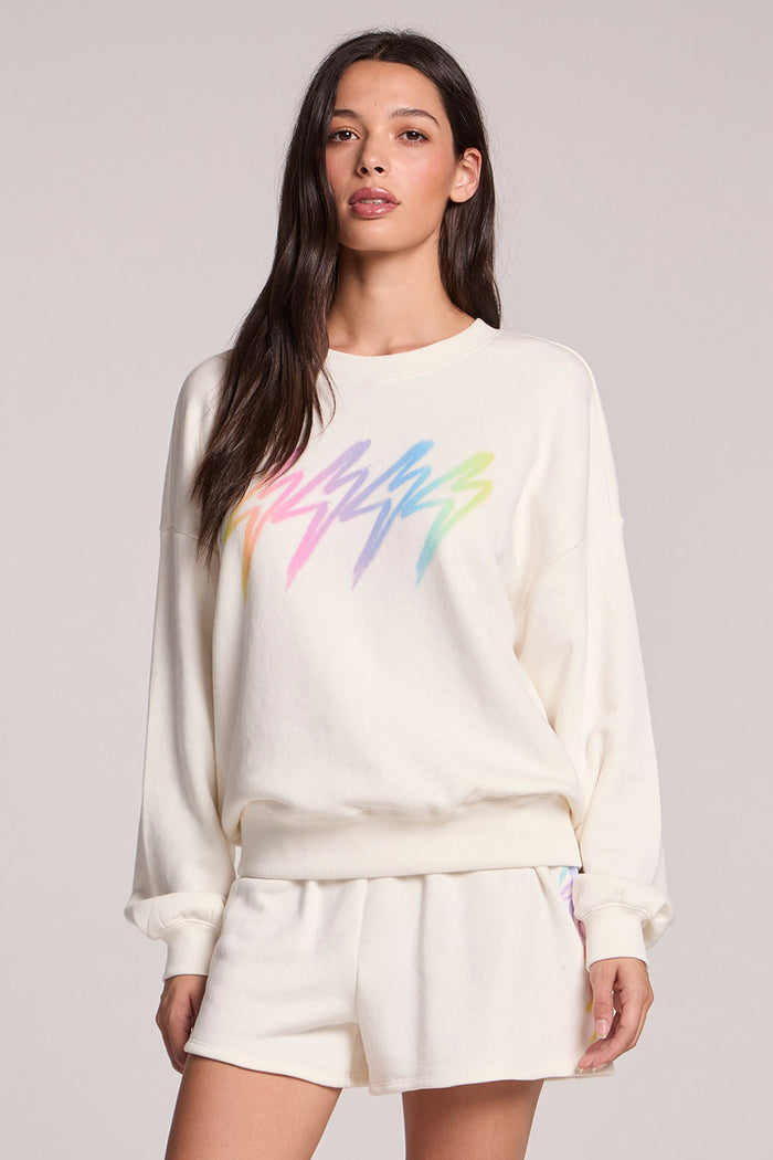 Front view of a woman wearing the Chaser Gradient Bolt Pullover and  shorts on a neutral background
