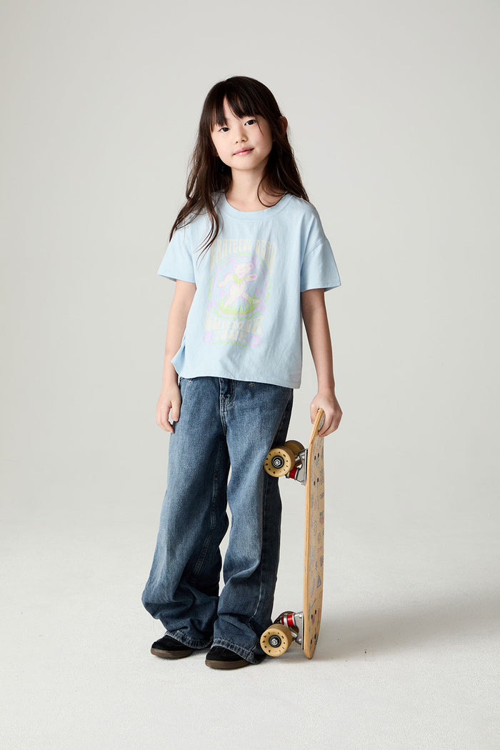 Image of a girl wearing the Chaser Grateful Dead In The Park Girls Tee on a neutral background standing holding a skateboard