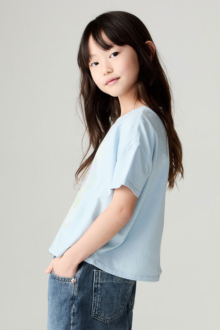 Side image of a girl wearing the Chaser Grateful Dead In The Park Girls Tee on a neutral background with jeans and hands in pockets