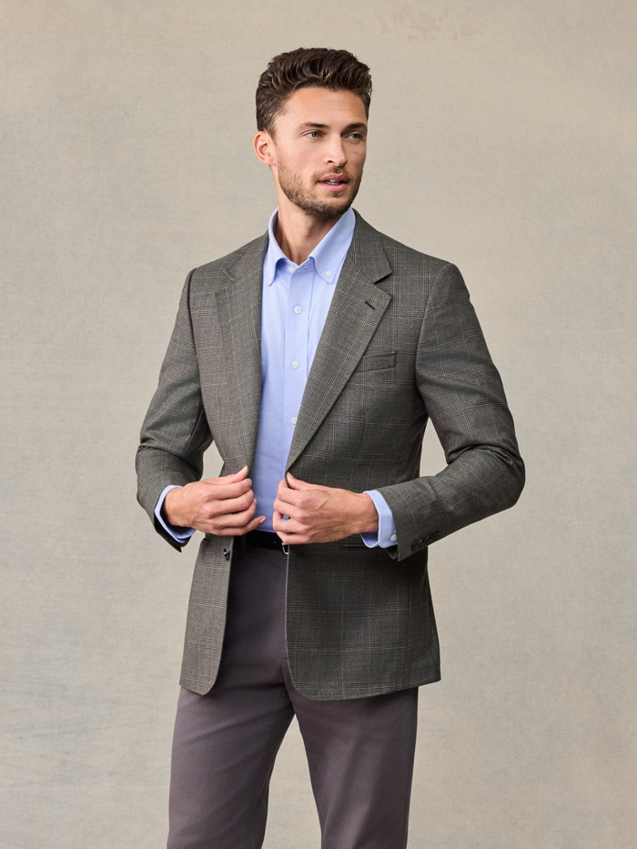 Man in a grey plaid sportcoat with a light blue shirt, unbuttoning the jacket.