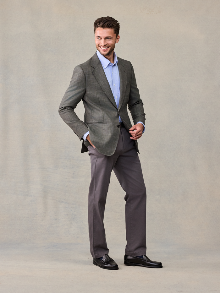 Smiling man in a grey plaid sportcoat with a light blue shirt, hand in pocket.