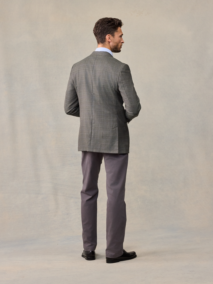 Back view of a man in a grey plaid sportcoat and grey trousers, walking.