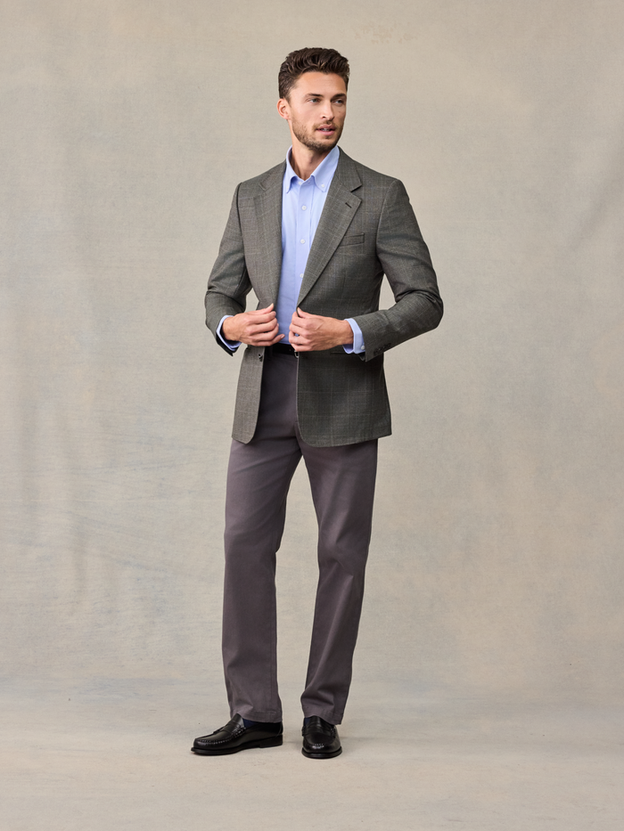 Man in a grey plaid sportcoat with a light blue shirt, adjusting the lapels.