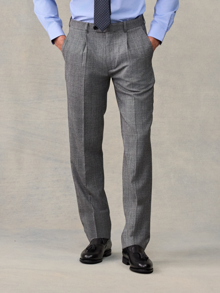 Man from waist down wearing grey plaid suit trousers, hands in pockets.