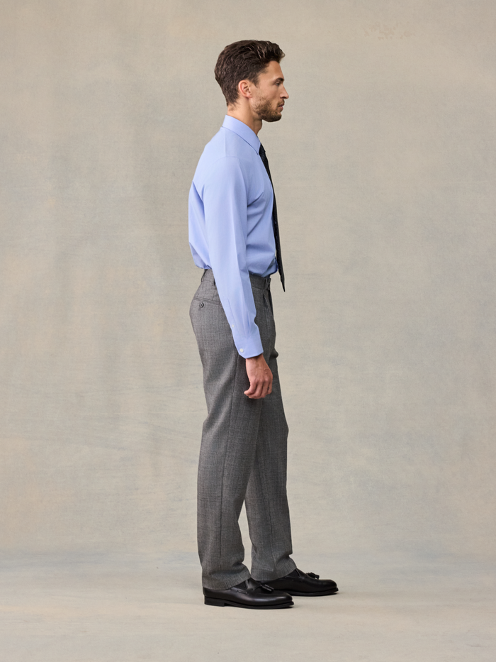 Side profile of a man in a light blue shirt and grey plaid trousers.