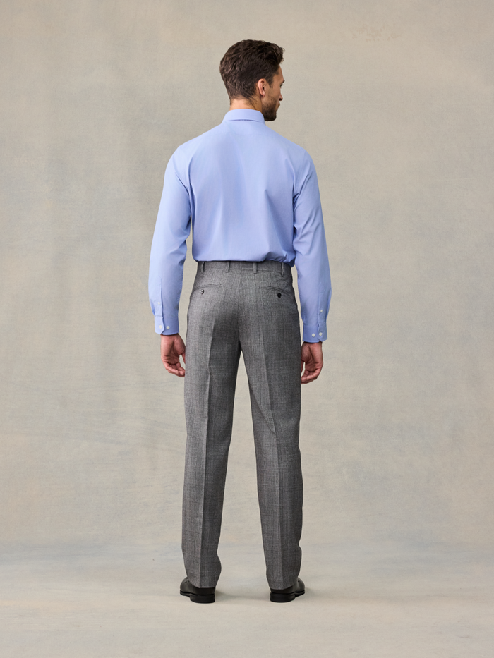 Back view of a man in a light blue shirt and grey plaid trousers.