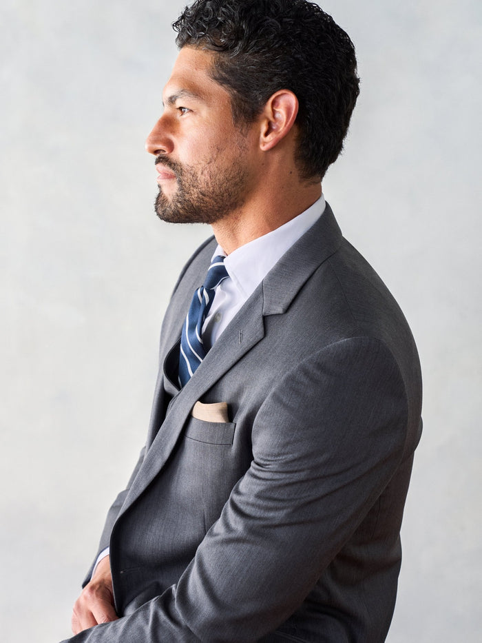 Side profile close-up of a man in a grey suit with a navy striped tie.
