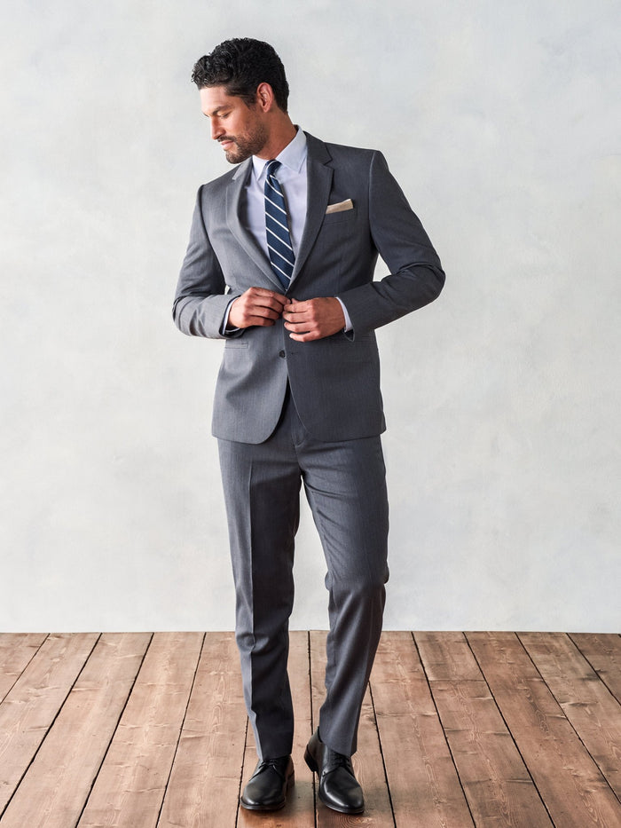 Man in a grey suit with a navy striped tie, buttoning the jacket.