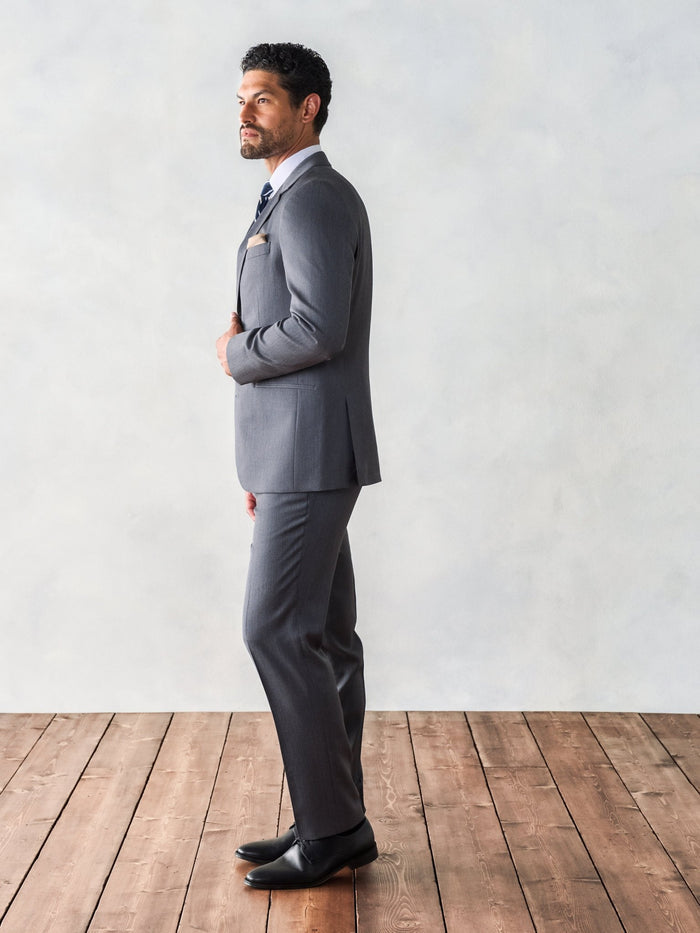 Side profile of a man in a grey suit with arms crossed.