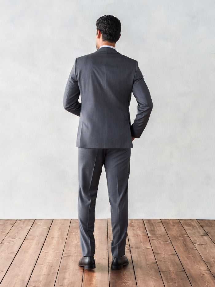 Back view of a man in a grey suit, standing.