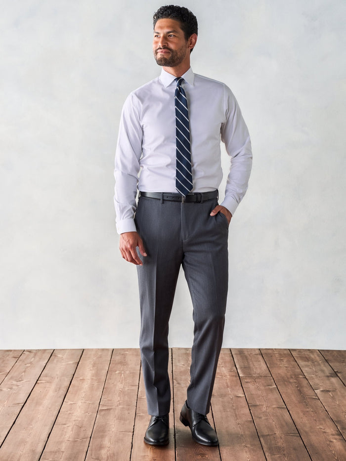 Man in white dress shirt, navy striped tie, and grey suit trousers, standing on wood floor