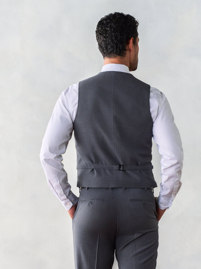 Back view of man in grey vest with adjustable strap buckle over white dress shirt