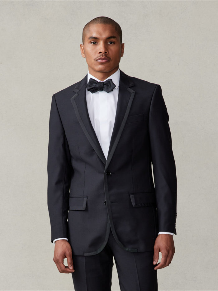 Man in black tuxedo with satin-edged lapel and black bow tie, cropped at waist