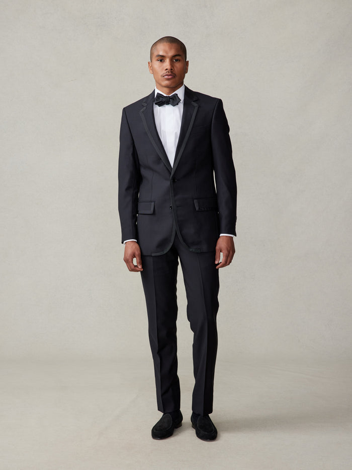 Man in black tuxedo and bow tie, standing full-length with hands at sides