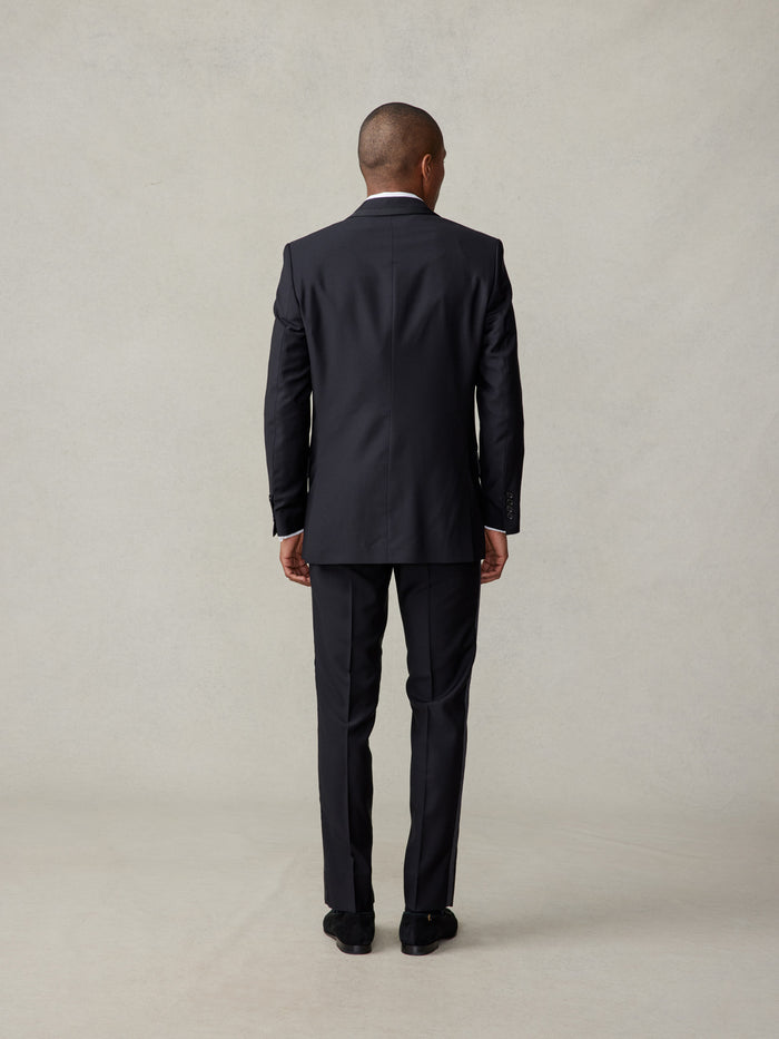Back view of man in black tuxedo jacket, full-length, against beige backdrop