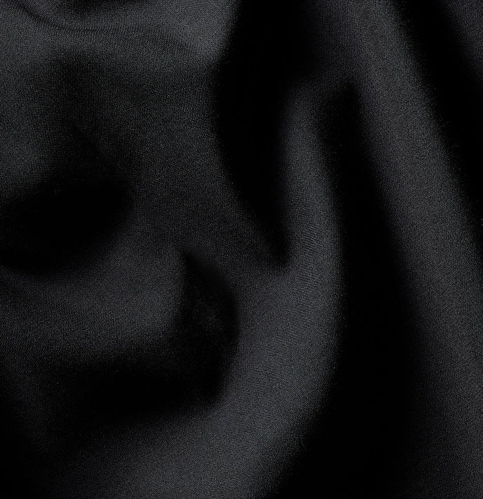 Close-up of black tuxedo jacket fabric, folds catching a subtle sheen