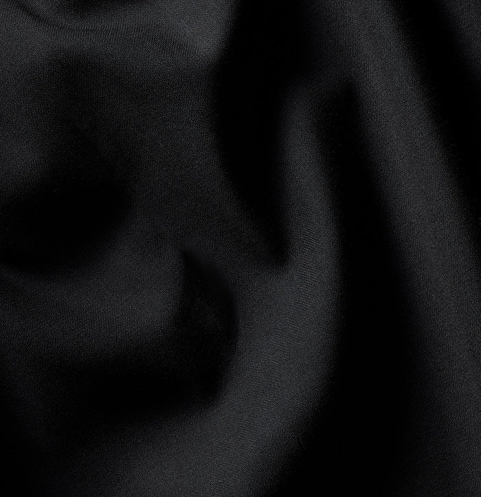 Close-up of black tuxedo trousers fabric, folds catching a subtle sheen