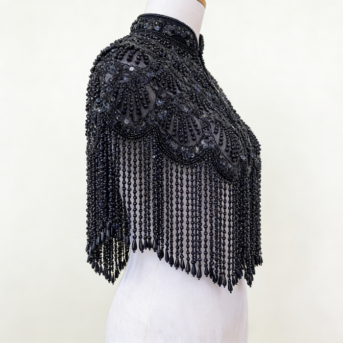 Handmade black bridal capelet featuring intricate bead embroidery, shimmering sequins, and cascading beaded fringe.