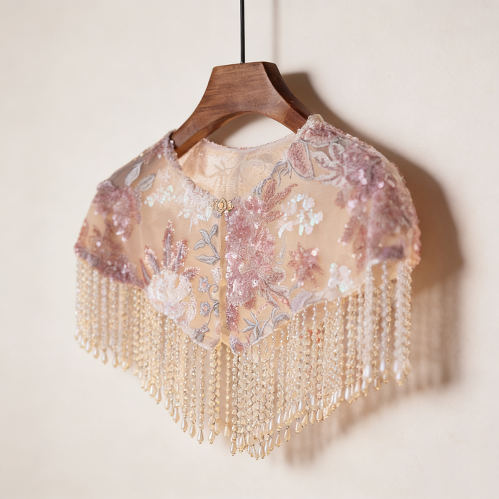 Handmade blush floral bridal cape featuring embroidered flowers, sequins, illusion tulle, and pearl-inspired fringe.