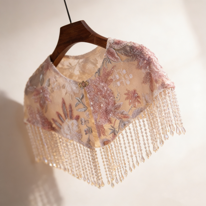 Handmade blush floral bridal cape featuring embroidered flowers, sequins, illusion tulle, and pearl-inspired fringe.