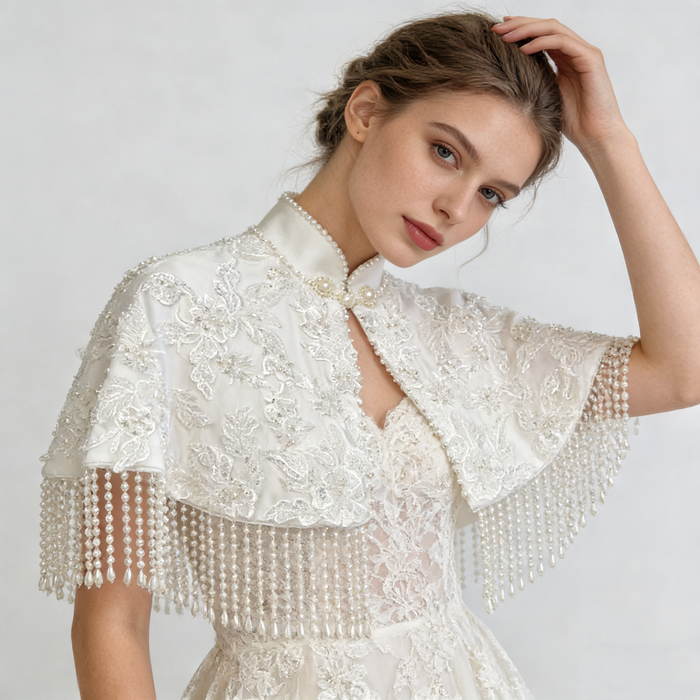 Handmade bridal cape featuring dimensional floral lace, hand-sewn bead embroidery, shimmering sequins, and elegant pearl-inspired fringe.