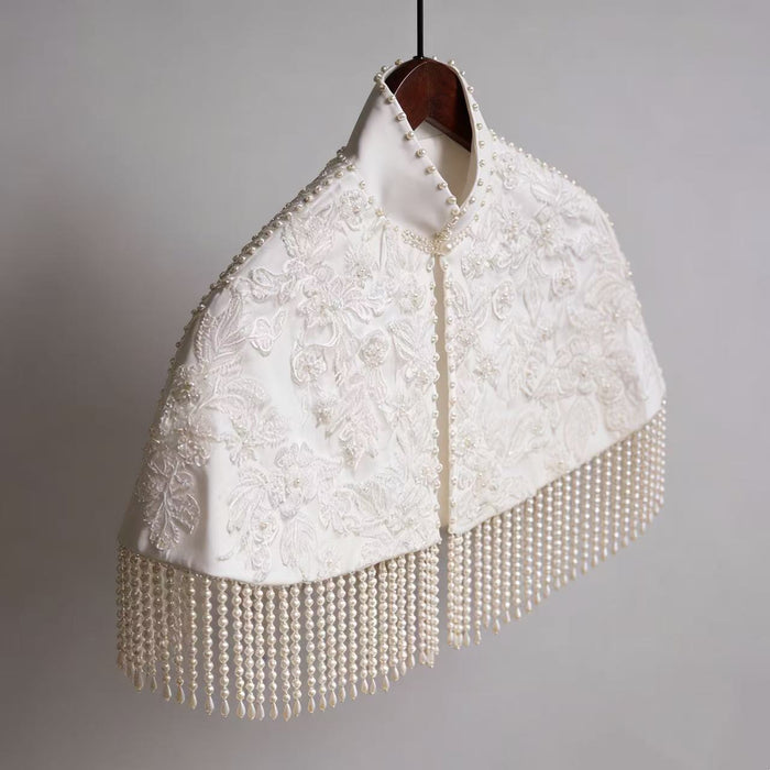 Handmade bridal cape featuring dimensional floral lace, hand-sewn bead embroidery, shimmering sequins, and elegant pearl-inspired fringe.
