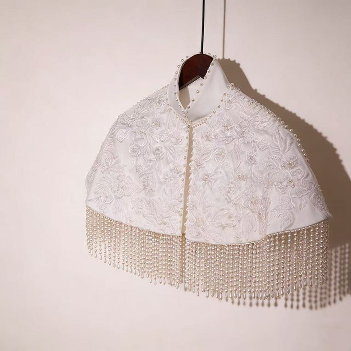 Handmade bridal cape featuring dimensional floral lace, hand-sewn bead embroidery, shimmering sequins, and elegant pearl-inspired fringe.