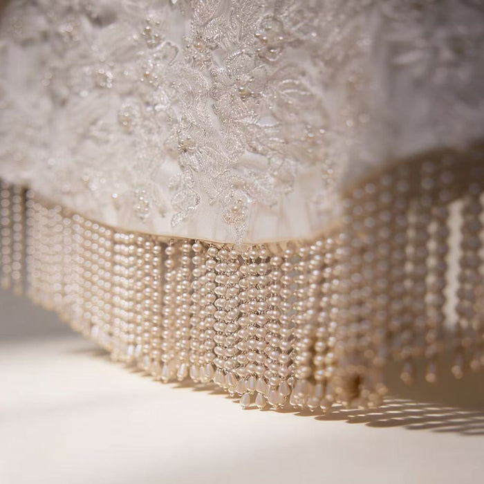 Handmade bridal cape featuring dimensional floral lace, hand-sewn bead embroidery, shimmering sequins, and elegant pearl-inspired fringe.