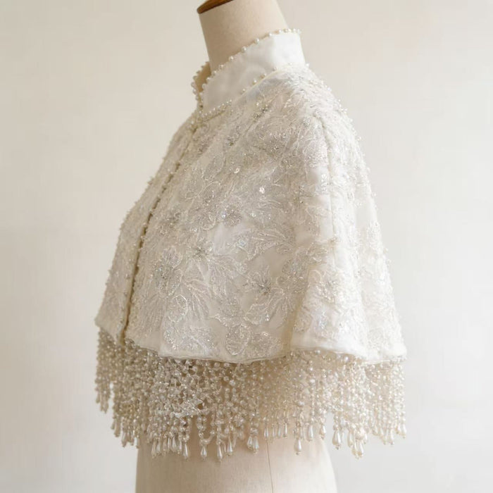 Elegant detachable bridal shoulder cape with three-dimensional floral lace, couture beadwork, satin finish, and cascading pearl fringe.