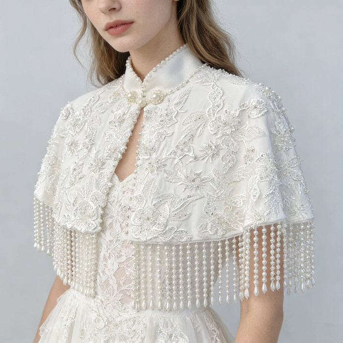 Elegant detachable bridal shoulder cape with three-dimensional floral lace, couture beadwork, satin finish, and cascading pearl fringe.