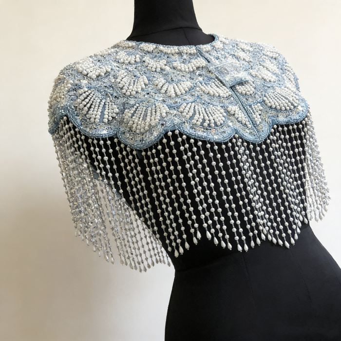 Handmade ice blue bridal cape with iridescent sequins, pearl bead embroidery, and cascading pearl-inspired fringe.