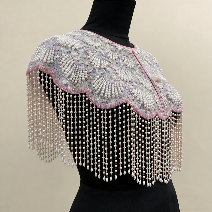 Handmade bridal cape featuring iridescent sequins, pearl bead embroidery, blush trim, and cascading pearl-inspired fringe.