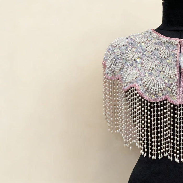 Handmade bridal cape featuring iridescent sequins, pearl bead embroidery, blush trim, and cascading pearl-inspired fringe.