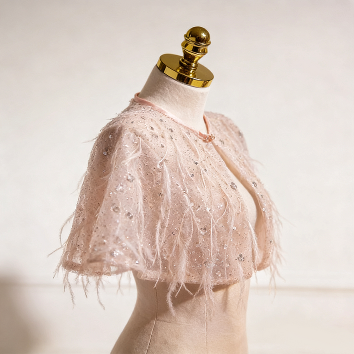 Handmade nude bridal capelet featuring illusion tulle, shimmering sequins, and soft feather embellishments.