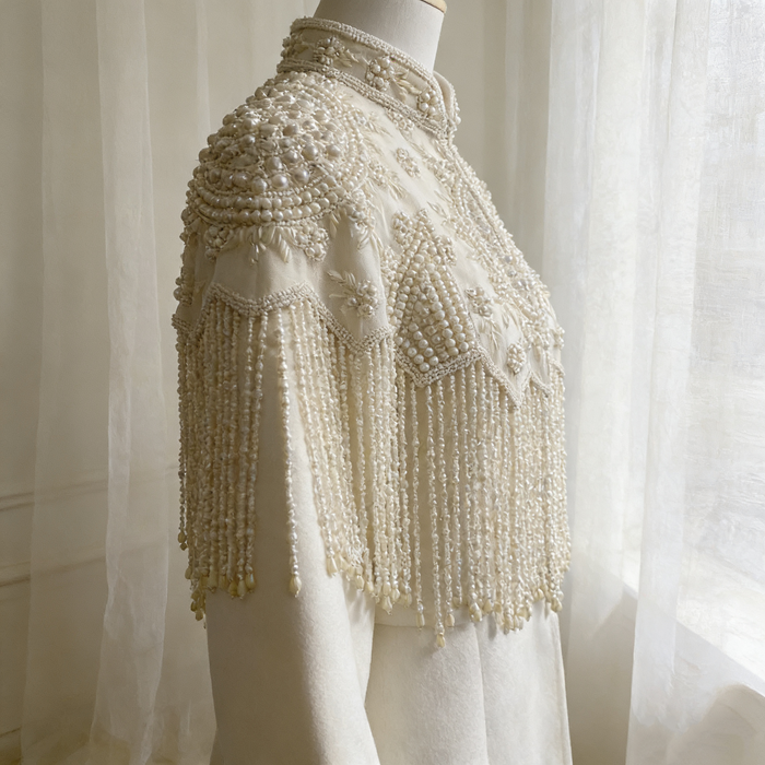 Handmade illusion tulle bridal cape embroidered with faux pearls, floral beadwork, and elegant pearl fringe.