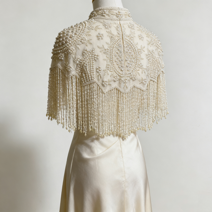 Handmade illusion tulle bridal cape embroidered with faux pearls, floral beadwork, and elegant pearl fringe.