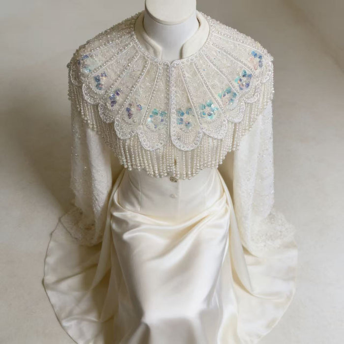 Handmade bridal cape featuring hand-sewn sequin bead embroidery, iridescent floral details, and cascading faux pearl fringe.