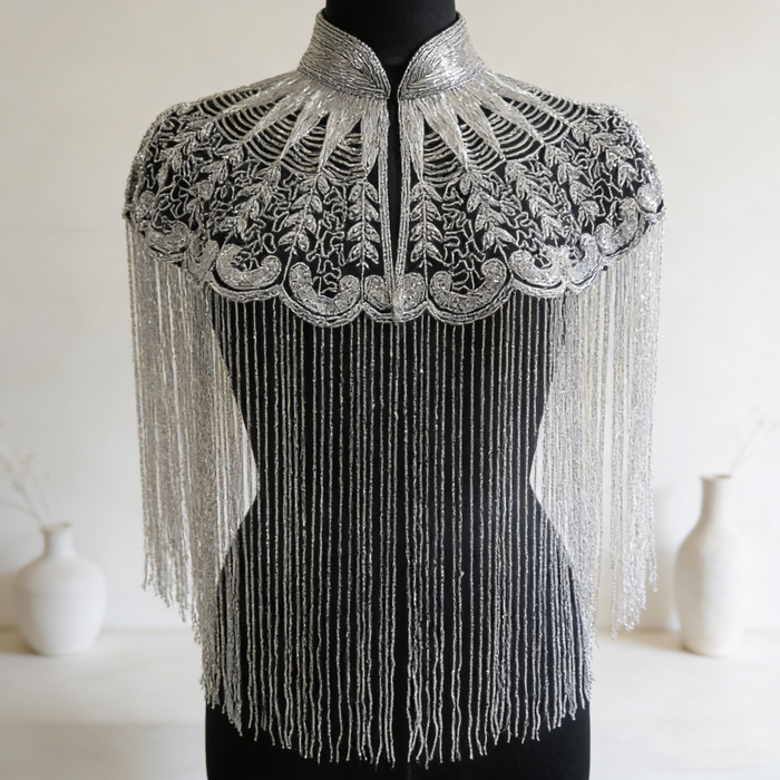 Handmade silver bridal cape featuring intricate bead embroidery, shimmering sequins, seed beads, and flowing metallic fringe.