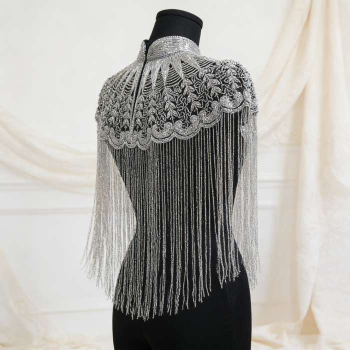 Handmade silver bridal cape featuring intricate bead embroidery, shimmering sequins, seed beads, and flowing metallic fringe.