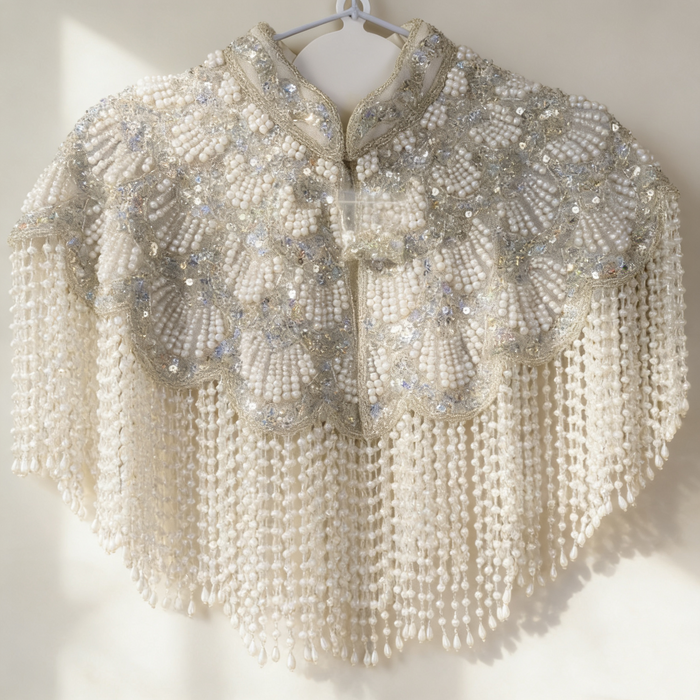 Handmade silver white bridal cape featuring pearl bead embroidery, shimmering sequins, and cascading pearl-inspired fringe.