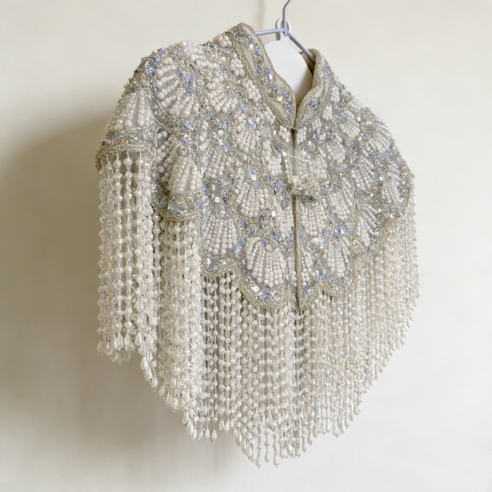 Handmade silver white bridal cape featuring pearl bead embroidery, shimmering sequins, and cascading pearl-inspired fringe.