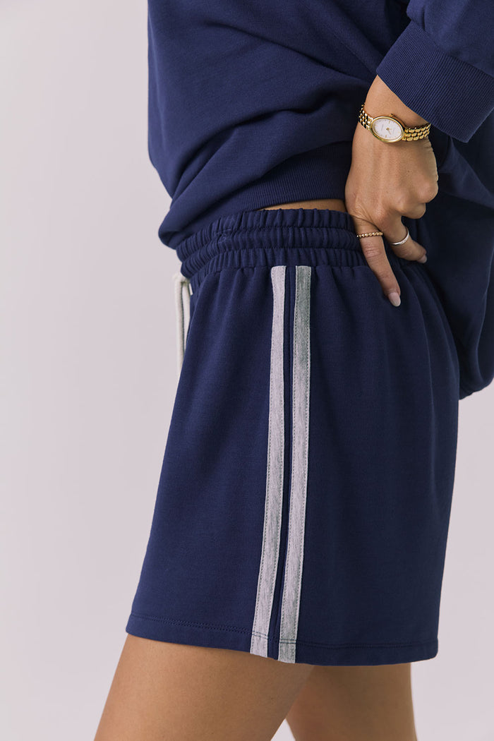 Side view of a woman wearing Chaser's navy blue Cornell Sapphire & Heather Grey Hanoverr shorts on a plain background