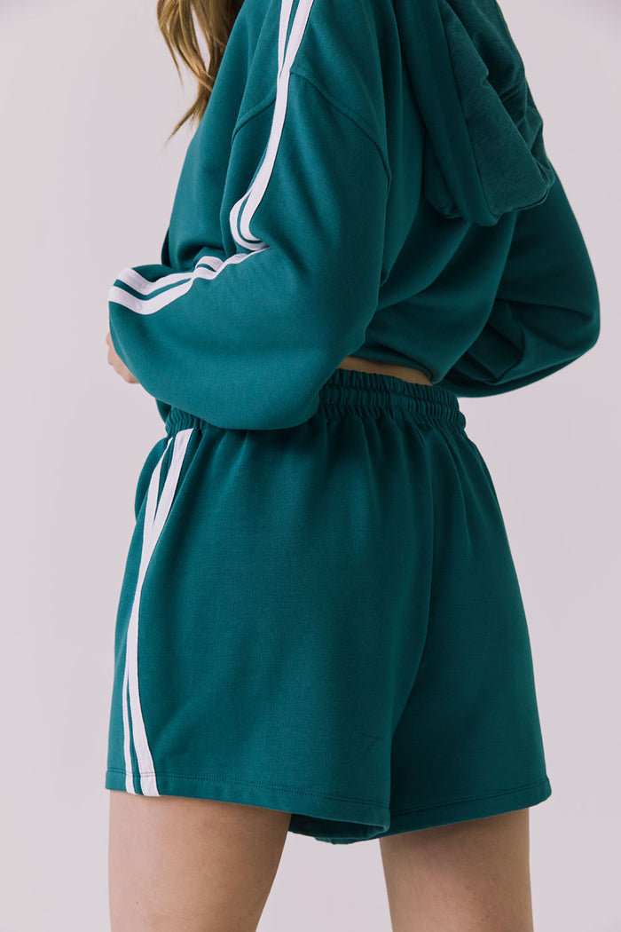 Back view of a woman wearing Chaser's Hanoverr Teal and White Shorts in a clean full body against a plain background