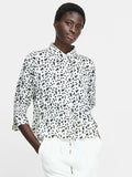 A woman wearing a cream button down shirt with a black floral pattern, 3/4 length sleeves, a collared neckline, and a self tie drawstring waist.