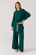 Full body view of woman wearing Chaser’s Hazel Joggers in Blue Grass Green with matching Cello Blue Grass Green Pullover on a white background
