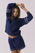 Front view of woman wearing Chaser's navy blue Heart Stitches Pullover Hoodie with the matching Heart Stitches Shorts on a plain background