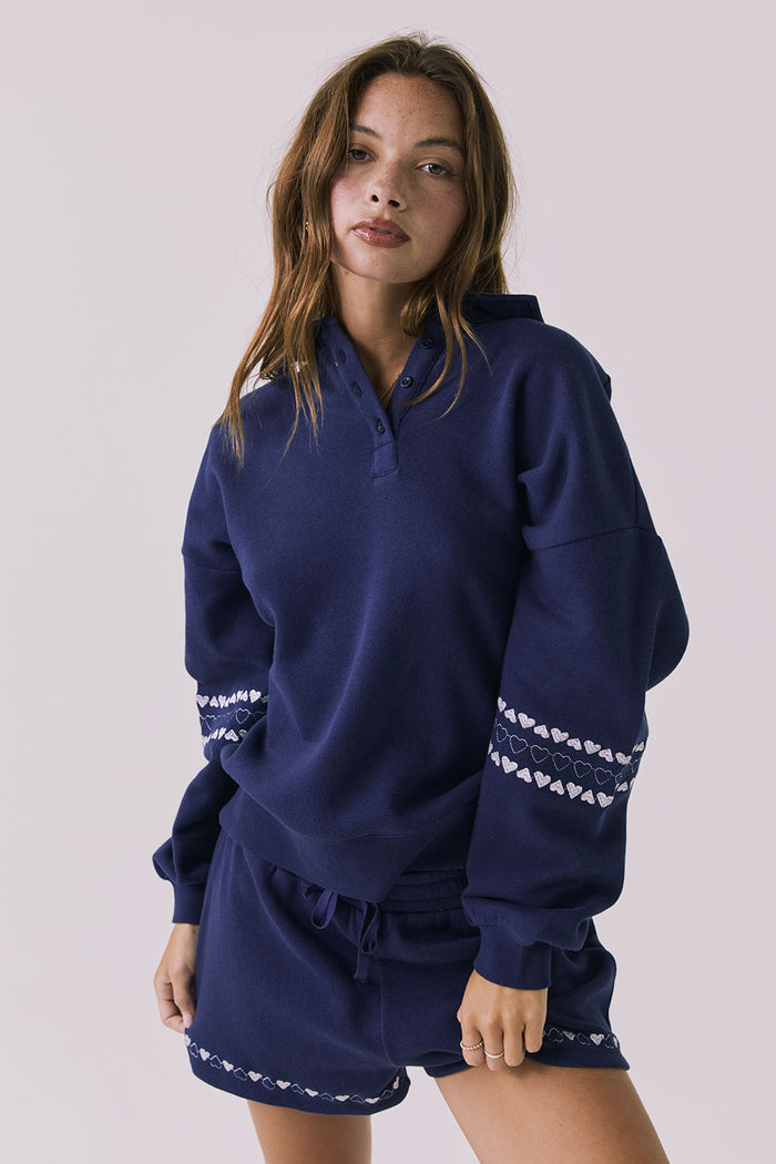 Front view of woman wearing Chaser's Heart Stitches Pullover Hoodie with the matching Heart Stitches Shorts on a plain background