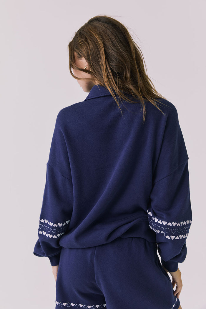 Back view of woman wearing Chaser's navy blue Heart Stitches Pullover Hoodie on a plain background