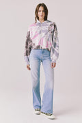 Full body view of woman wearing Chaser’s Heart Tie Dye Zip Up Hoodie with light blue jeans on a white background